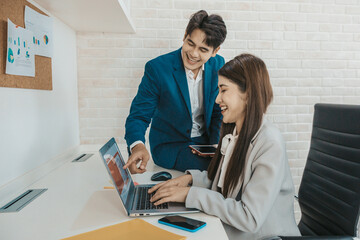 Business couple sitting together checking work  while using laptop in office.