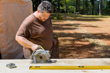 The worker holds a circular saw in his hand while cutting plywood with he is using