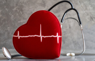 Close up photo of red heart, stethoscope and heart rate graph in the same frame. Concept of cardiovascular health and illnesses.