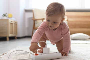 Cute baby playing with power strip on floor at home. Dangerous situation