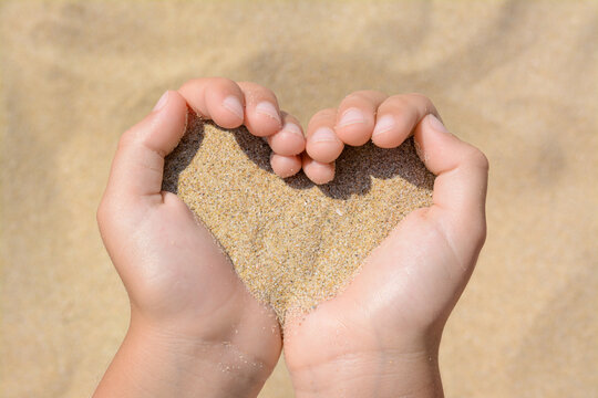 Child holding sand in hands outdoors, closeup. Fleeting time concept