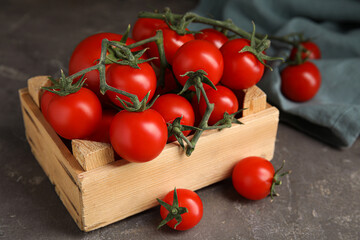 Many ripe red tomatoes in wooden crate on grey table