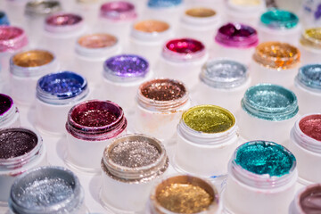 Colorful makeup glitters in plastic cosmetic jars in row on counter for sale in makeup store, exhibition - close up, selective focus. Glamour, fashion, make up, beauty and skincare concept