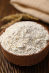 Bowl of organic wheat flour on wooden table, closeup