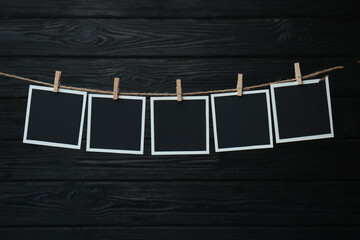 Clothespins with empty instant frames on twine against black wooden background. Space for text