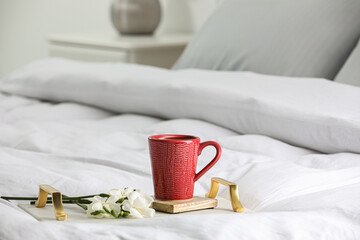 Fototapeta na wymiar Mug of hot drink with stylish cup coaster and beautiful freesia flowers on bed in room