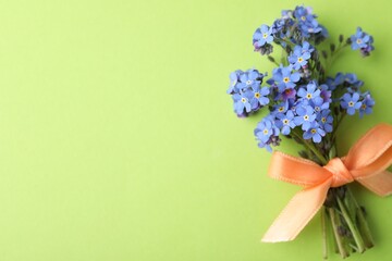 Beautiful blue forget-me-not flowers tied with ribbon on light green background, top view. Space for text