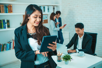 Portrait of a beauty indian business woman CEO smiling. Portrait of a positive looking young business professional standing holding tablet with co-workers talking in the background.