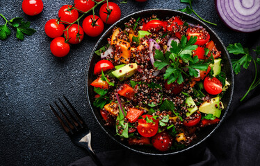Quinoa tabbouleh salad with tomatoes, paprika, avocado, cucumbers, onion and parsley. Traditional Middle Eastern and Arabic dish. Black kitchen table background, top view