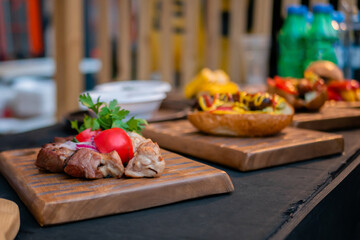 Shish kebab, tomato and hot dog with sausage on wooden board on table at outdoor street food festival, market. Gastronomy, sale and takeaway food concept