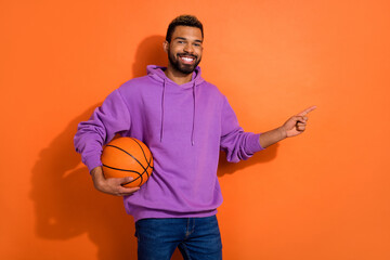 Photo of cheerful nice person hold basketball indicate finger empty space isolated on orange color background