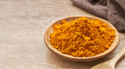 a pile of ground turmeric powder or curcumin powder in wood plate on wooden table background. turmeric or curcumin powder background                                                         