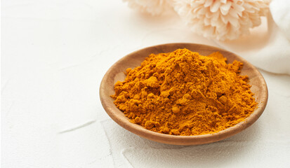 a pile of ground turmeric powder or curcumin powder in wood plate on white table background. turmeric or curcumin powder background                                                             