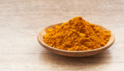a pile of ground turmeric powder or curcumin powder in wood plate on wooden table background. turmeric or curcumin powder background                                                         