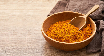 close up a pile of ground turmeric powder or curcumin powder in wood plate and scoop on wooden table background. turmeric or curcumin powder                                           