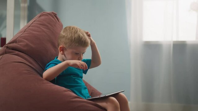 small child sits in room in armchair against background of window
