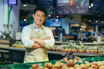 portrait of a happy handsome Asian salesman. Vegetables and fruits at the market or grocery store....