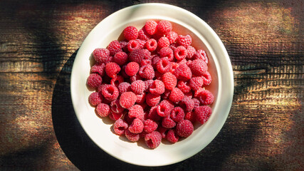 Raspberry berries. Top view raspberries in a plate on a wooden background. Selective focus. Shallow depth of field.