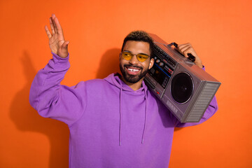 Photo of carefree positive person carry boombox listen music dance isolated on orange color background