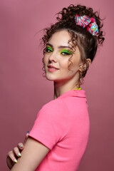 Young woman on pink background with green eyes makeup and curly hair.