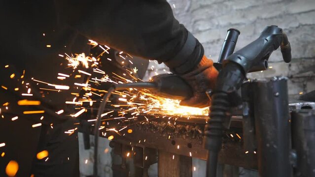 Craftsman use saw cutting machine to cut metal detail. Man with circular saw sawing steel in garage or workshop. Industrial professional worker grinding metal. Sparks fly from hot metal. Slow motion