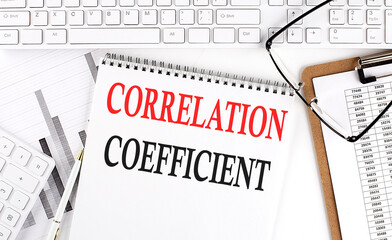 Text CORRELATION COEFFICIENT on Office desk table with keyboard, notepad and analysis chart on white background.