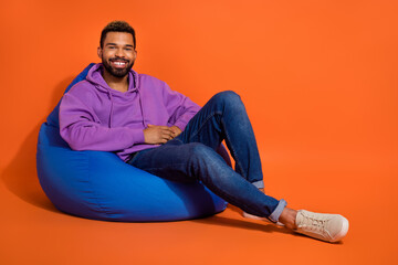 Full body photo of peaceful carefree man sit comfy bag have good mood isolated on orange color background