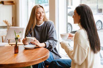 Two young women smiling and drinking tea while sitting at cafe