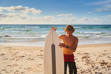 Fototapeta na wymiar Shirtless man carrying surfboard at the beach against clear sky and wavy ocean