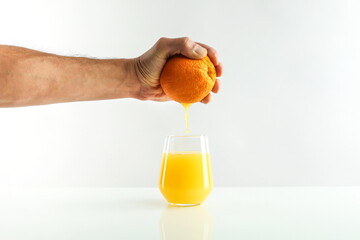 concept of freshly squeezed orange juice. hand squeezes juice from orange into a glass. fresh orange juice flowing into a glass on white background