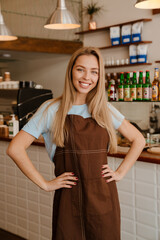 Fototapeta na wymiar Blonde young waitress woman wearing apron smiling while working at cafe