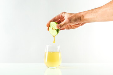 concept of freshly squeezed apple juice. hand squeezes juice from apple into a glass. juice flowing into a glass on white background