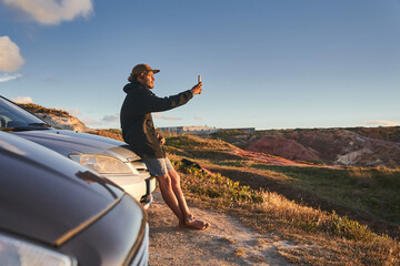Curly young man taking selfie portrait at the beach near his car