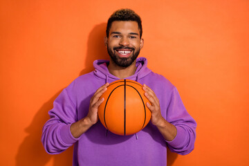 Photo of positive cheerful man arms hold basketball toothy smile isolated on orange color background