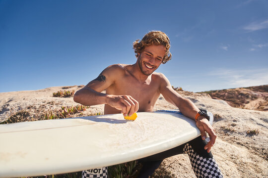 Healthy man waxing surfboard surface at the beach