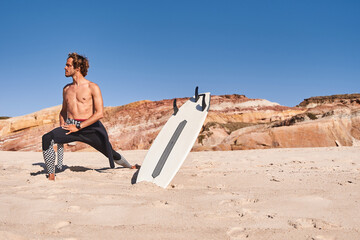 Surfer sportsman stretching body while standing at the beach and looking at water