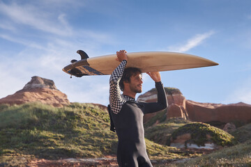 Handsome young man looking directly at the water with smile while holding his surfboard