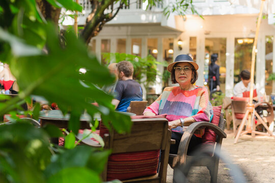 Portrait of senior woman in straw hat sitting on a chair in cafe outdoor.