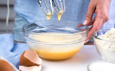 A young woman beats eggs with a mixer at the kitchen at home. Biscuit making process. Selective focus.