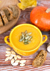 Seasonal pumpkin cream soup and baked rye bread on a wooden table. Close-up.