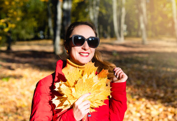 Hello, Autumn! Happy young woman with a bouquet of autumn yellow leaves in the park. Sunny autumn day. Selective focus.