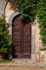 Wooden door in medieval town in Tuscany, Italy. Old stone walls and plants