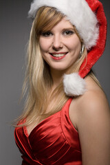 young pretty blonde christmas woman with santa claus hat  in front of a grey background