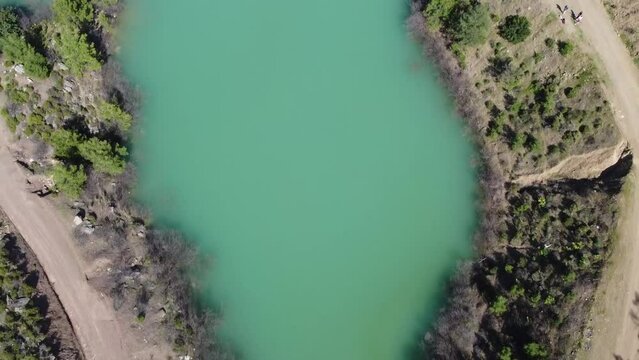 Blue lake next to a dirt road and forest, aerial photography with a drone