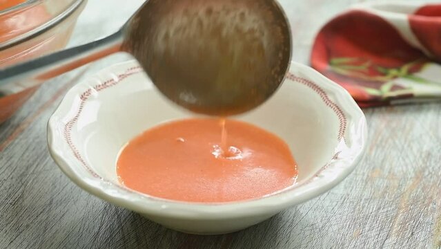 The cook pours the cold tomato soup into the bowl.
