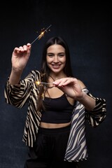 A beautiful young woman in a smart shirt and trousers with sparklers. Selective focus on the hands.
