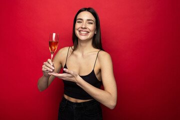 Smiling young woman with a glass of champagne on a red background.