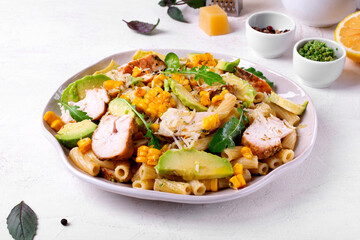 Pasta salad with chicken, avocado, grilled corn, cheese, arugula and pesto sauce served on the...