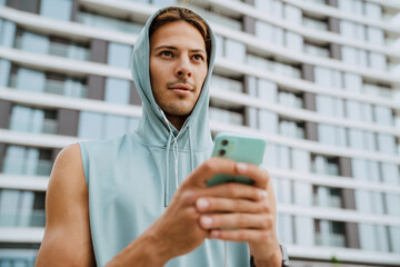 Young athletic long-haired serious handsome man in hood with phone