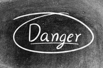 White chalk hand writing in word danger on blackboard background
